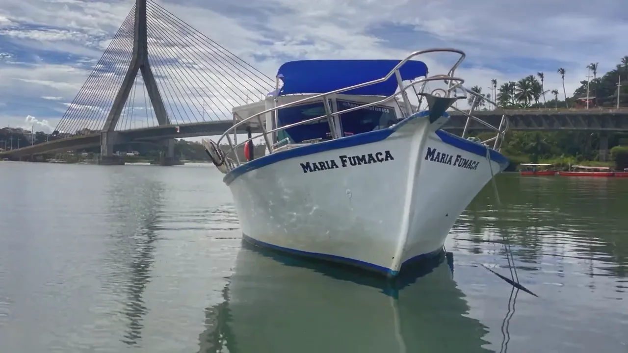Barco Maria Fumaça ancorado no rio, com a ponte de Ilhéus ao fundo